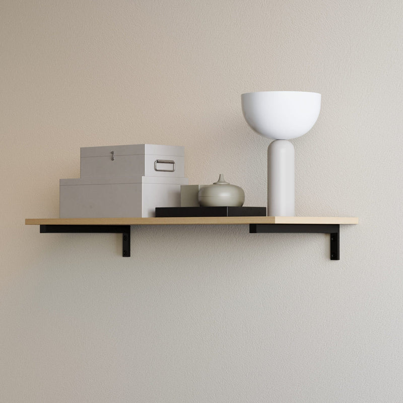 Holzregal mit schwarzen Halterungen an hellbeiger Wand, darauf zwei graue Aufbewahrungsboxen, schwarze Platte, weiße Vase und kleine graue Dekoration