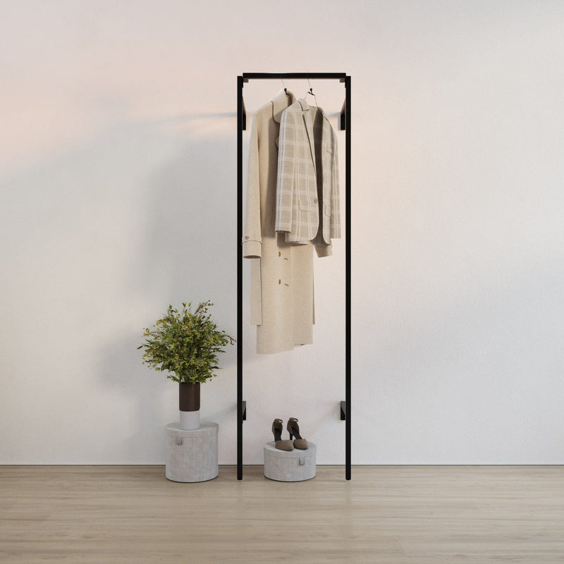 Schlichter schwarzer Kleiderständer mit hellen Kleidungsstücken, daneben Pflanze auf zylindrischem Beistelltisch vor weißer Wand