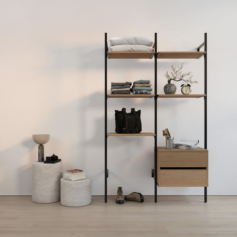 Schwarzes Metallregal mit Holzablagen, darauf Kissen, gefaltete Kleidung, Vasen, Wecker und geschlossenes Schuhpaar auf hellem Boden vor weißer Wand