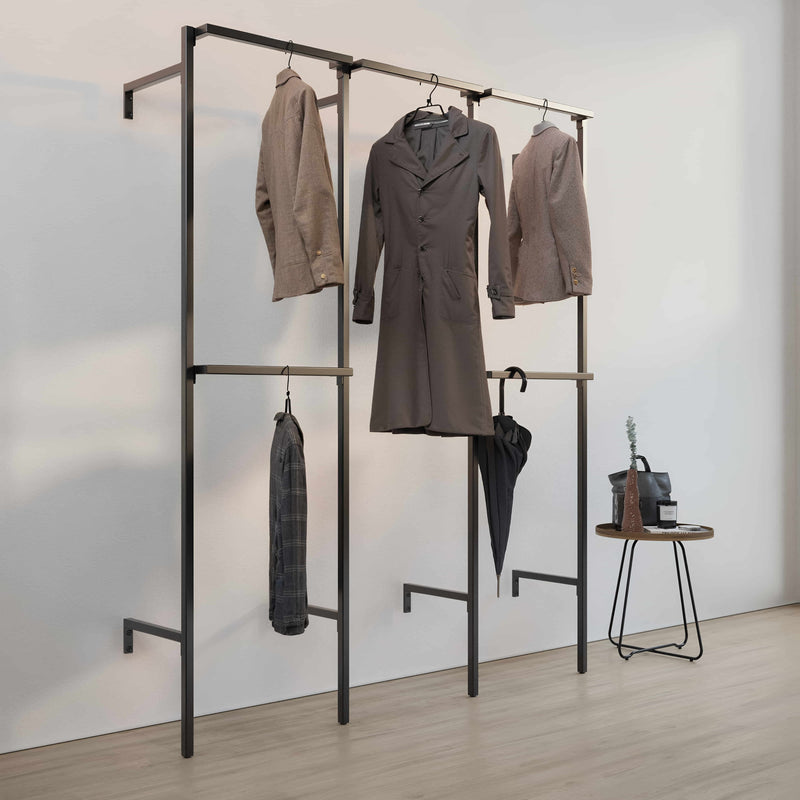 Schwarzes Garderobenständergestell mit drei Jacken, Regenschirm und kleinem Tisch mit Tasche und Vase in schlichtem Raum