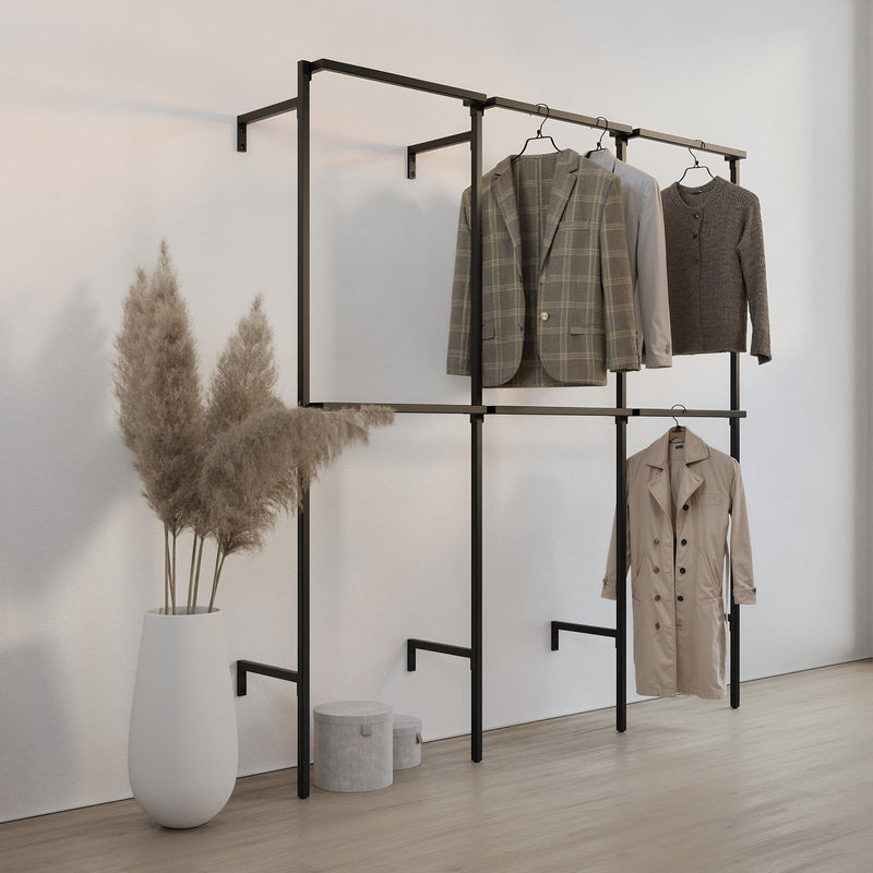 Schwarzes Metallgestell mit verschiedenen Kleidungsstücken und dekorativem Pampasgras in hellem Raum mit Holzboden