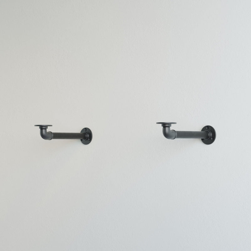 Helle Wand mit zwei schwarzen, industriellen Halterungen aus Metall im minimalistischen Stil montiert