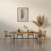 Hell beiger Raum mit Holztisch, vier Stühlen, Pflanzenarrangement und Bild einer Feder an der Wand