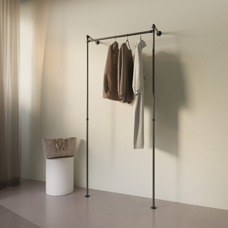 Minimalistische schwarzer Kleiderständer mit drei hellen Kleidungsstücken vor beiger Wand und weichem Lichtschein