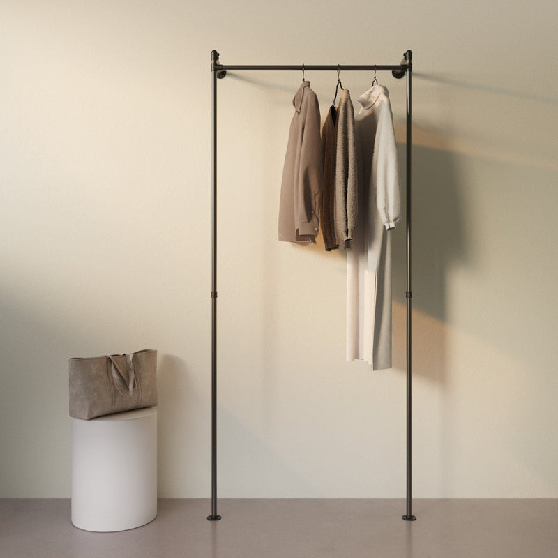 Minimalistische Garderobe mit drei Kleidungsstücken in neutralen Tönen an schwarzem Kleiderständer vor hellem Hintergrund