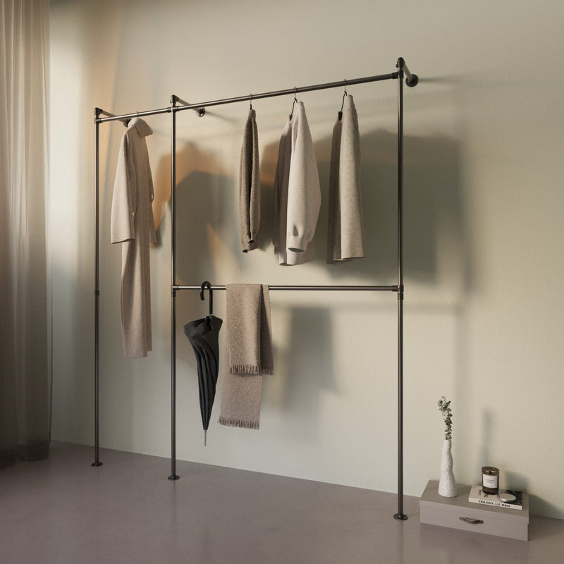 Minimalistische Kleiderstange mit neutralen Kleidungsstücken, Schirm und Deko vor hellgrünem Hintergrund in schlichtem Raum