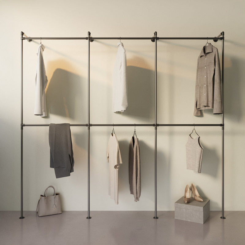 Minimalistisches Kleiderregal mit hellen Kleidungsstücken, Handtasche und Paar beiger Damenschuhe vor hellem Hintergrund