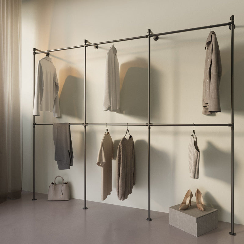 Minimalistische Kleiderstange aus Metall mit beiger Kleidung, Tasche und Schuhen vor beigeweißem Hintergrund in hellem Raumlicht